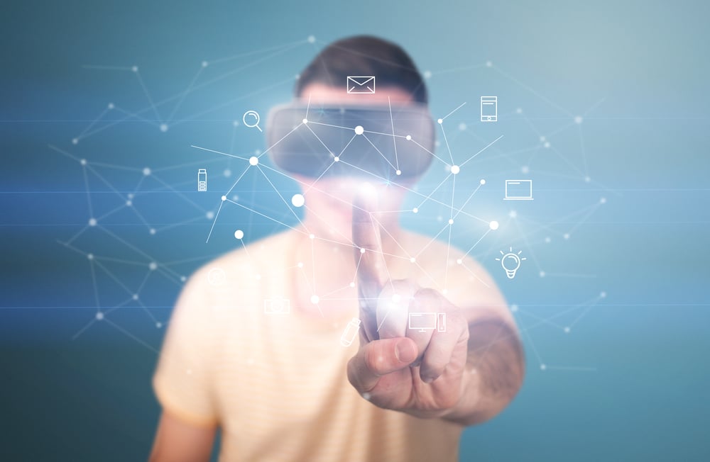 Young impressed man wearing virtual reality goggles with mixed media icons around his finger